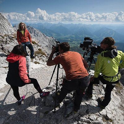 Filmteam mit Kamera auf Felsen bei Interview in den Bergen, professionelle Luftbildproduktion