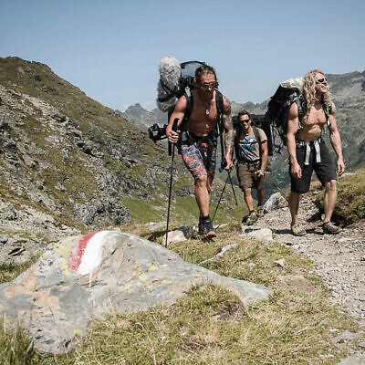 Drei Männer mit Kameratechnik und Rucksäcken wandern für Filmaufnahmen im alpinen Gebirge