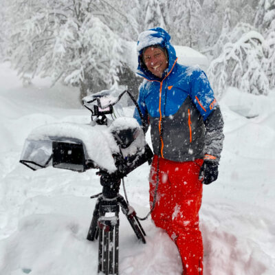 Kameramann mit Videokamera im verschneiten Wald, professionelle Filmproduktion im Winter