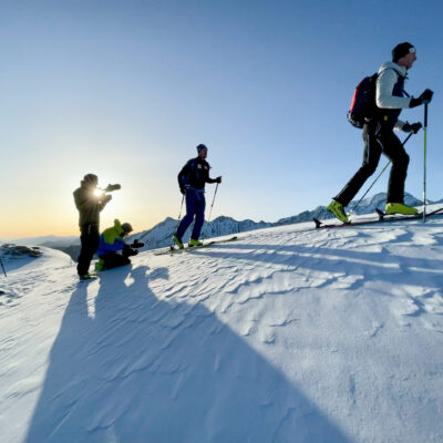 Skifahrer und Filmteam bei Sonnenaufgang auf verschneitem Bergrücken für Videoproduktion