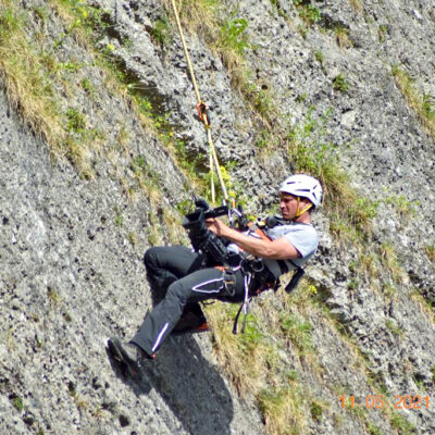 Kameramann mit Kletterausrüstung filmt an steiler Felswand, professionelle Luftaufnahmen Outdoor