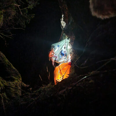 Höhlenforscher mit Helm und Ausrüstung bei Nacht, beleuchtet beim Abstieg in eine Felsspalte