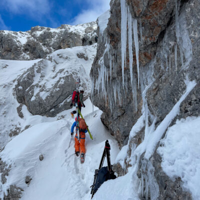 Bergsteiger mit Skiausrüstung am vereisten Fels, Kameraequipment für Luftaufnahmen im Schnee